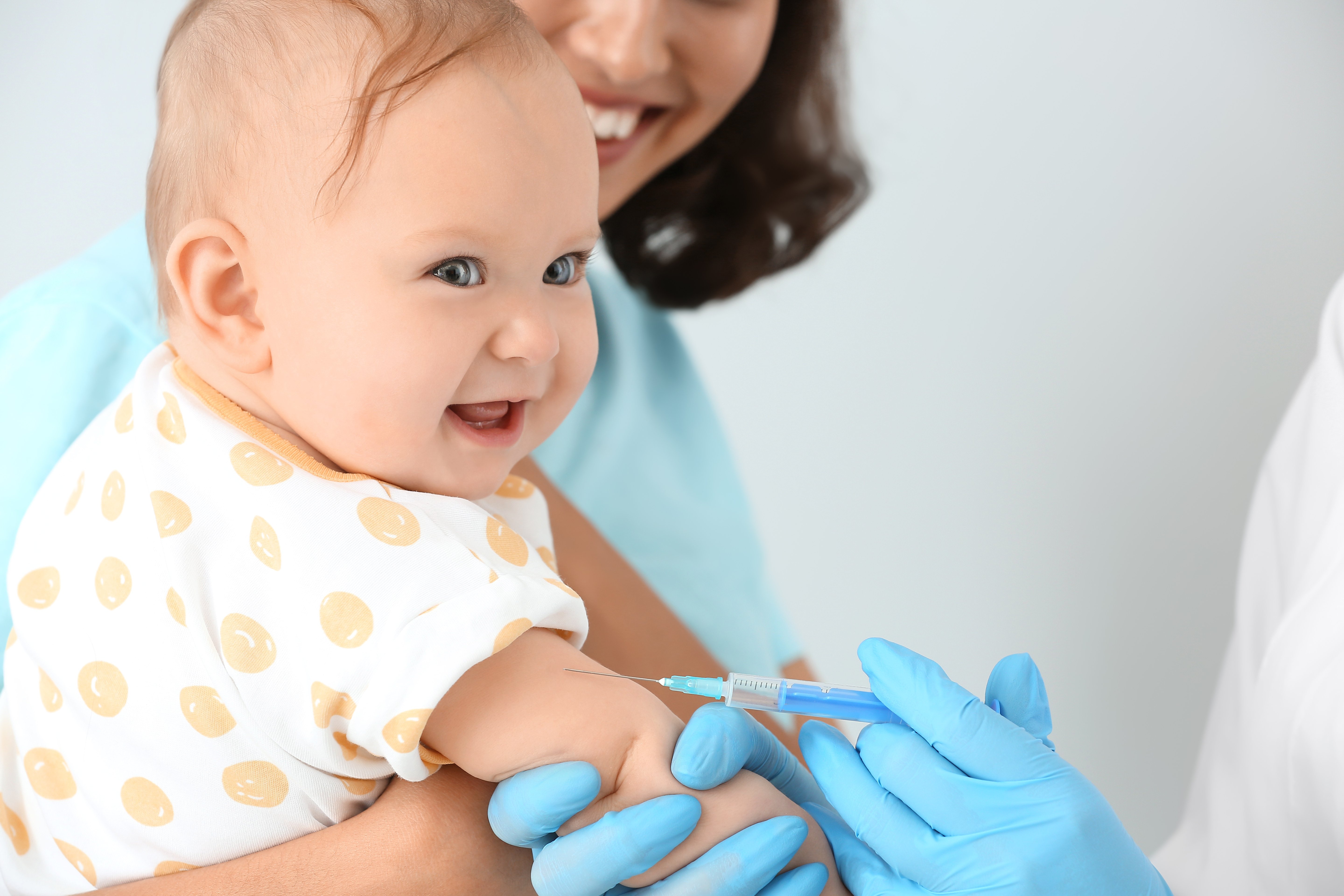  A smiling baby is getting vaccinated in the arm by a doctor while being held by a woman, with text that reads 'Contraindications to childhood immunization'.